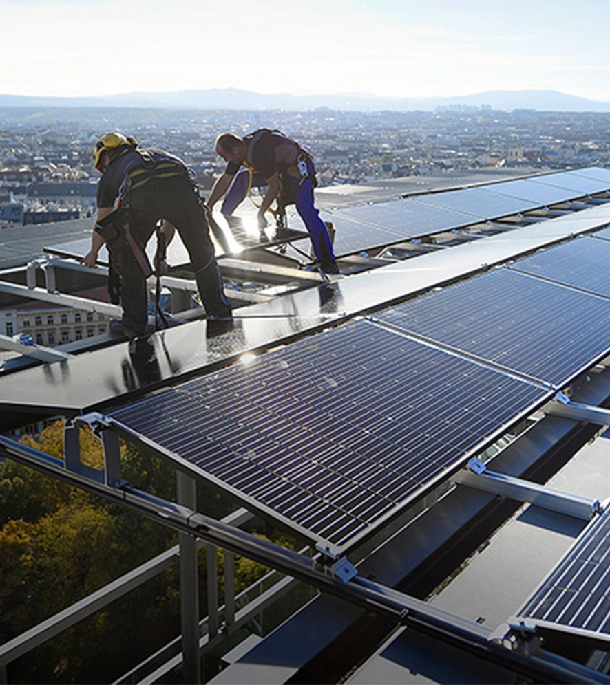 Zwei Mitarbeitende installieren Photovoltaik-Platten auf einem Gebäudedach in Wien. C: Johannes Zinner